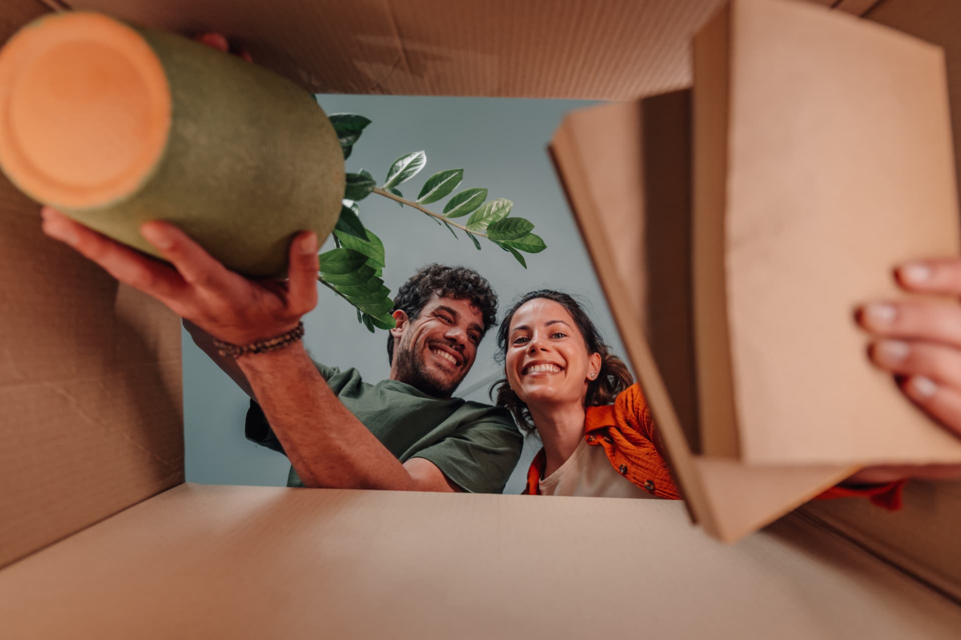Un couple déballant un carton de déménagement, un pot de plante à la main