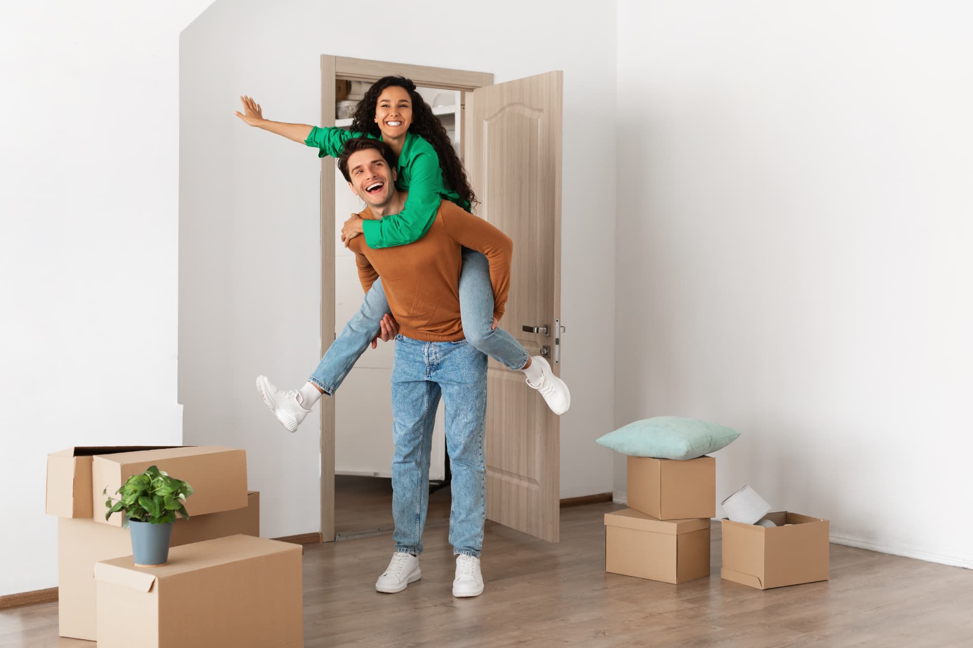 Un jeune couple emménage dans son nouvel appartement, l'un portant l'autre devant les cartons de déménagement